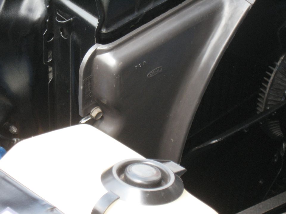 Engine bay with a white fluid reservoir and a dark grey fender liner showing a Ford logo