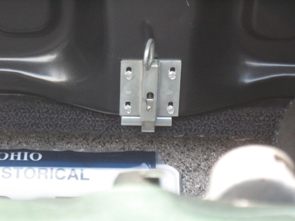 Close-up of a metal trunk latch assembly with a ring, mounted on a dark surface. A blue and white label with 'OHIO HISTORICAL' is visible below