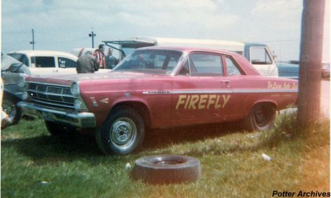 1967 Ford Fairlane - A vintage red Ford Fairlane, possibly a 1966 model, is parked on a grassy area with other vehicles in the background.