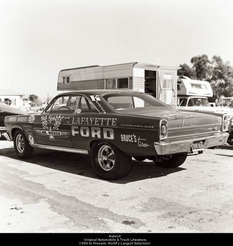 1967 Ford Fairlane - A dark 1966 Ford Fairlane race car is parked next to a trailer, displaying sponsor decals and racing slicks.