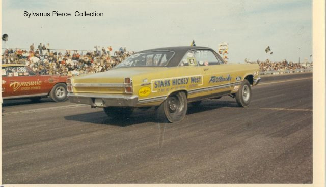 Yellow Ford drag car lifting front wheels at launch on a dragstrip, rear 3/4 view