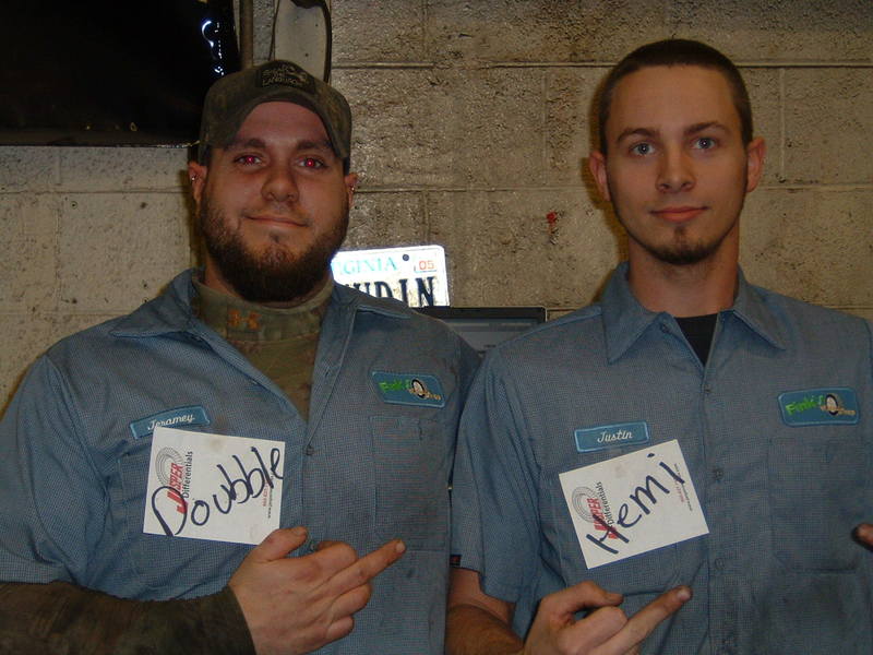 Two men in blue work uniforms, one with a beard and cap, the other clean-shaven, holding name tags that say 'Doubble' and 'Hemi'