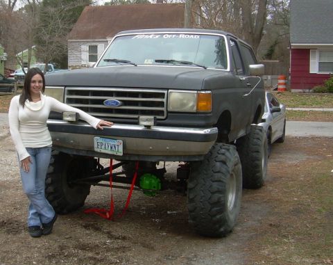 1979 Ford F-150 - A woman poses next to a heavily modified black Ford truck with oversized tires and a lifted suspension.