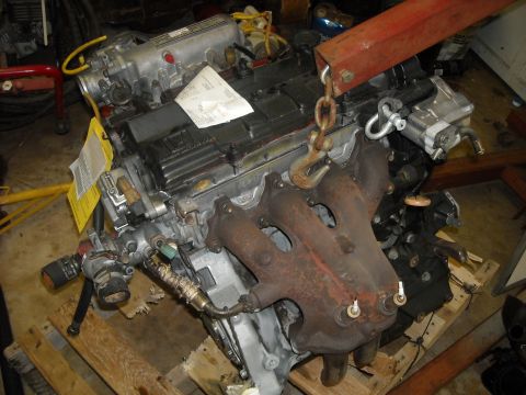 1979 Ford F-150 - Engine assembly suspended by a hoist, resting on wooden pallets.