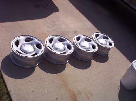 1988 Ford Bronco - Four silver wheels are laid out on a concrete surface under bright sunlight.