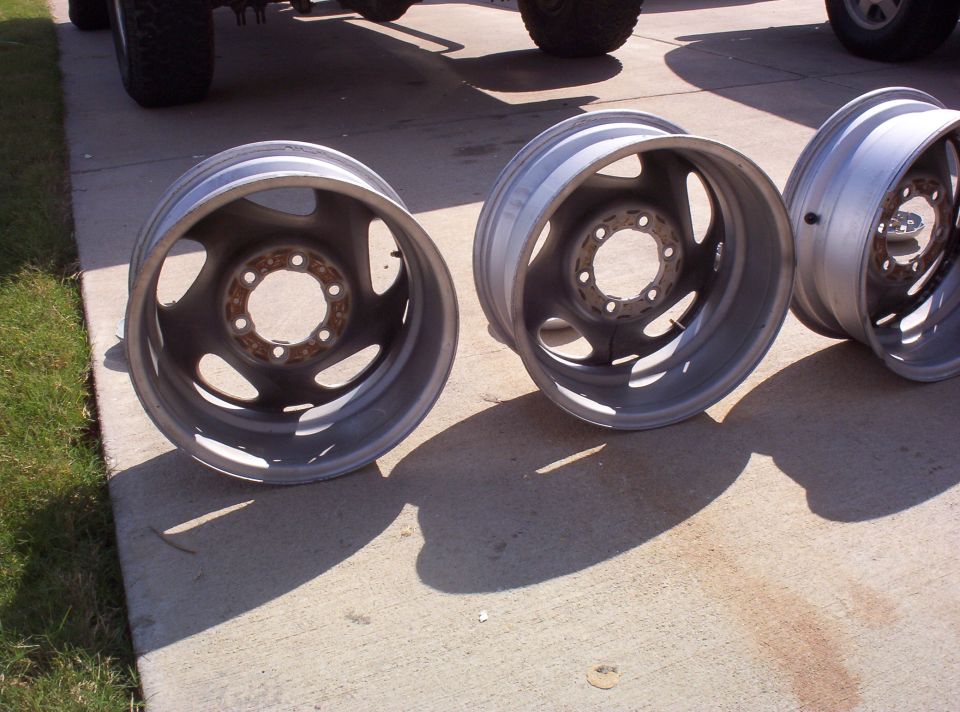 Three 8-lug five-slot alloy wheels standing on a concrete driveway, tires removed