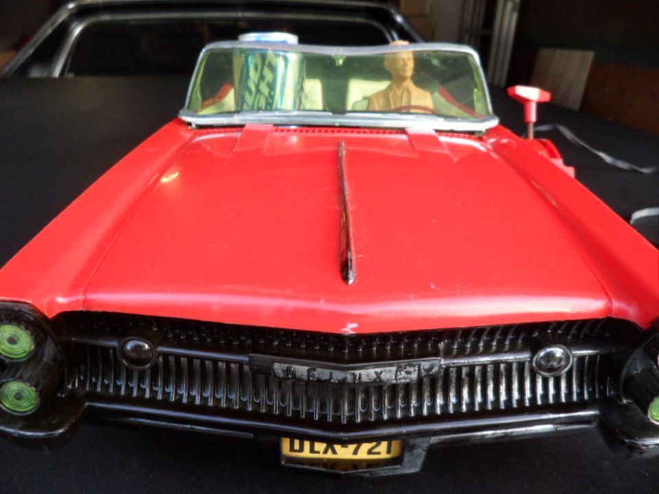 red toy car with a mannequin driver, parked behind a black vehicle