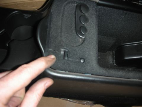 1998 Ford Crown Victoria - finger points to a molded mounting tab and cupholder area inside a black plastic center console storage bin.