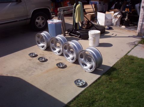 1988 Ford Bronco - A collection of four aluminum wheels and three hubcaps are laid out on a driveway.