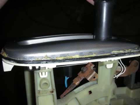 1998 Ford Crown Victoria - removed automotive interior trim assembly held by hand, showing a metallic mesh panel and a cream plastic housing with old adhesive residue.