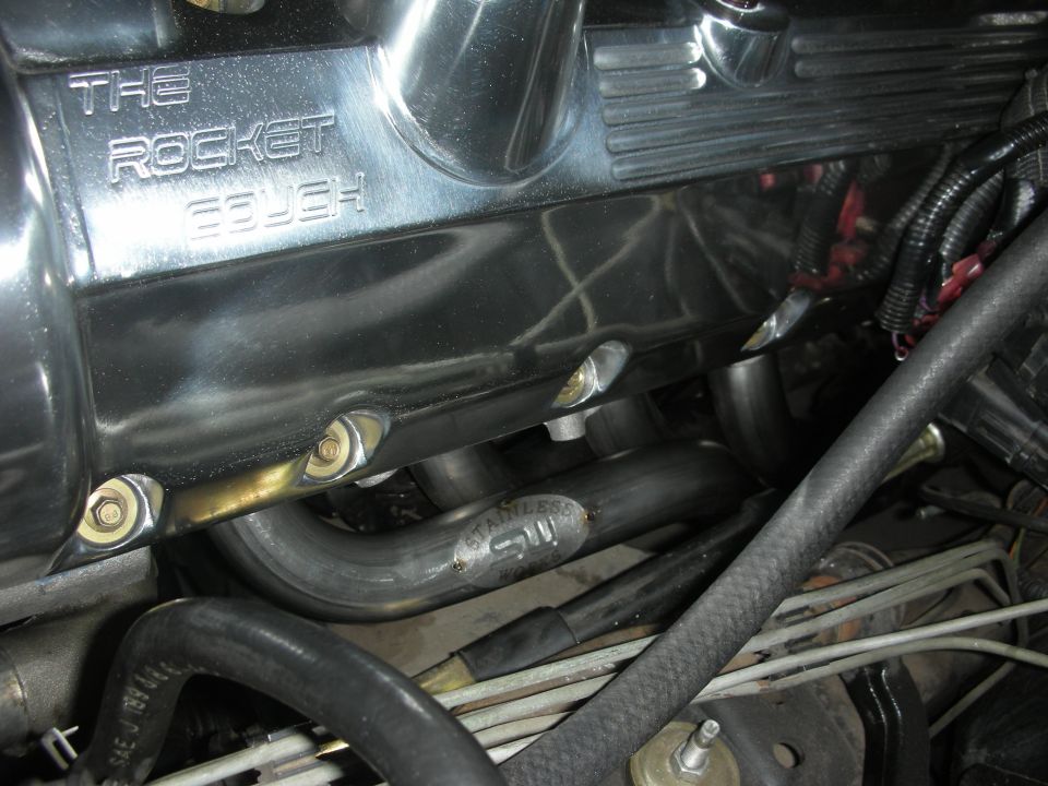 Chrome valve cover with 'THE ROCKET COUGH' engraved, connected to exhaust headers. Stainless steel pipe visible