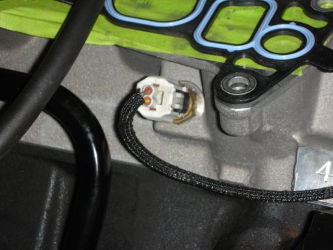 1992 Ford Crown Victoria - A close-up view of an engine sensor with a braided wire harness, next to a gasket on an engine block.