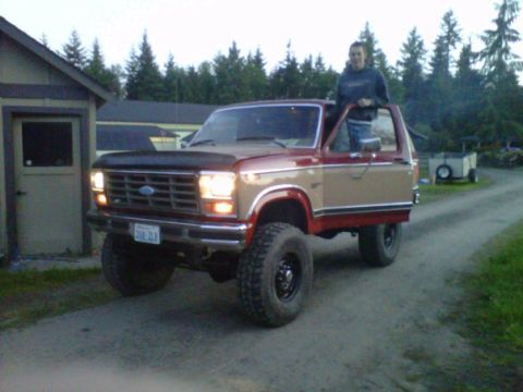 1984 Ford Bronco - This two-tone Ford Bronco has large tires and a person leaning out of the driver's side door.
