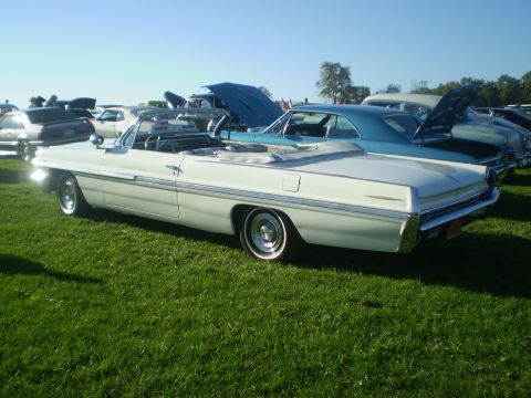 1979 Ford Bronco - A classic white convertible is displayed on a grassy field alongside other vehicles at an outdoor event.