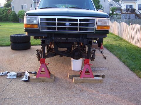 1992 Ford Bronco - Front view of a green 1992 Ford Bronco undergoing maintenance, with the front axle removed and the vehicle supported by jack stands.