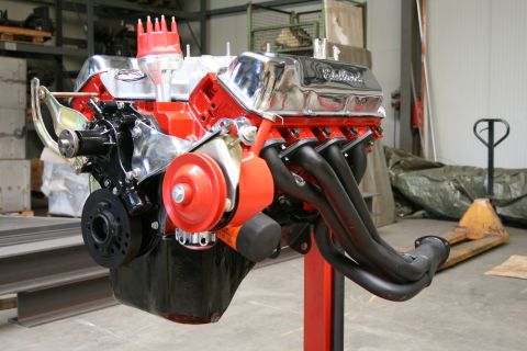 1973 Ford Ranchero - A V8 engine with chrome Edelbrock valve covers and black headers is displayed on a red stand.