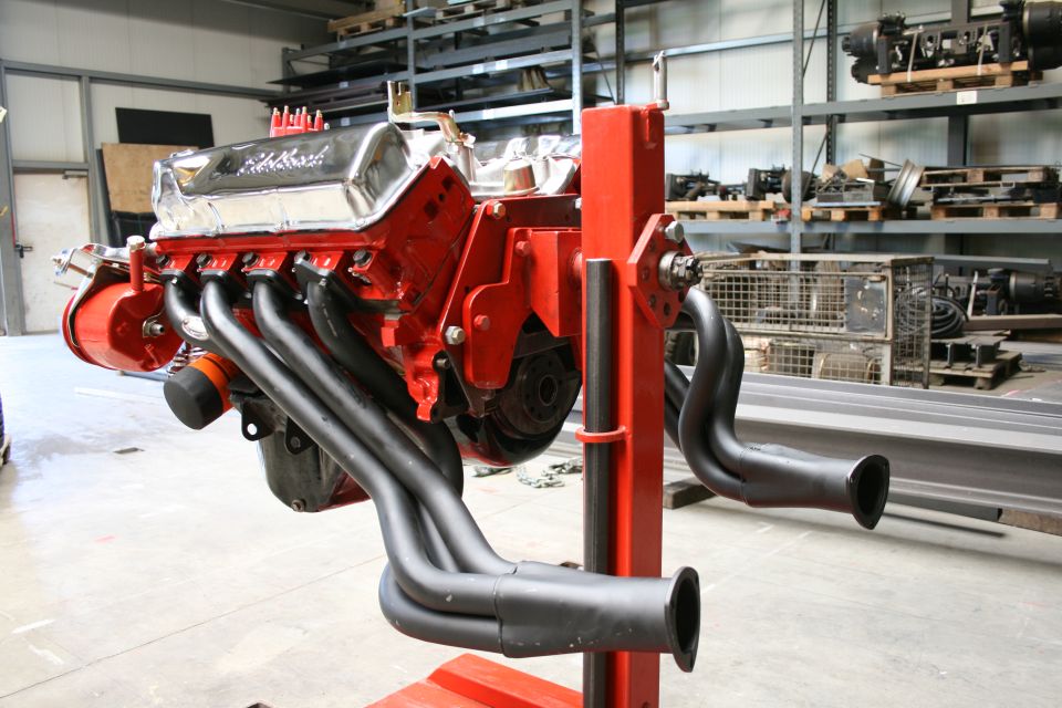 V8 engine on red stand, chrome valve covers, red block, black headers