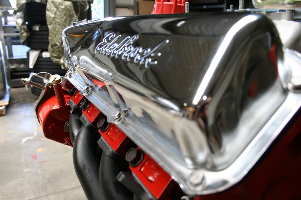 Chrome Edelbrock valve cover on a red engine block with black exhaust headers