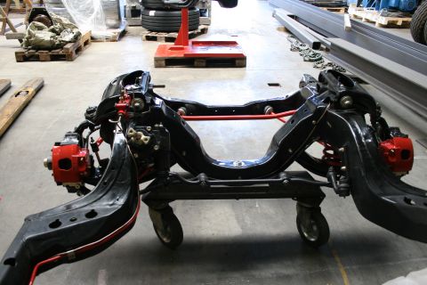 1973 Ford Ranchero - A vehicle's front subframe assembly, complete with suspension and brake components, rests on a wheeled cart in a workshop.