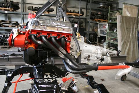 1973 Ford Ranchero - Engine and transmission assembly, Edelbrock valve covers and custom headers, is hoisted in a workshop setting.