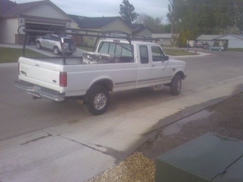 1989 Ford Bronco - White Ford F-250 pickup truck with a ladder rack and toolbox is parked in a driveway next to a house.