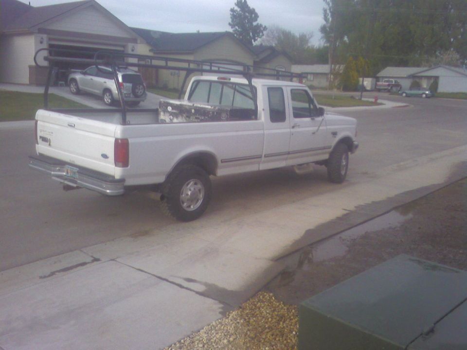 White Ford F-250 pickup truck with ladder rack and toolbox, parked in driveway. Silver SUV in garage