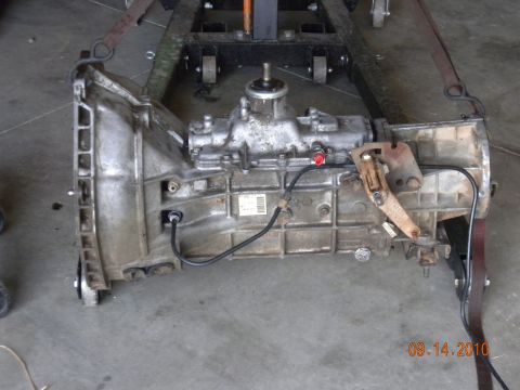 1989 Ford Bronco - A vehicle transmission is shown, suspended by straps on a stand in a workshop setting.