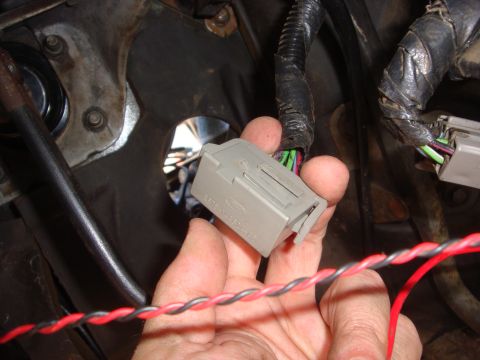 1989 Ford Bronco - A hand holds a gray electrical connector with the Ford logo visible, likely for a vehicle's wiring harness.