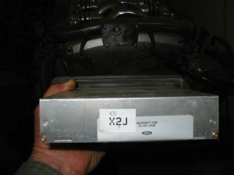 1993 Ford Taurus - A hand holds a Ford engine control module in its finned aluminum case, with the white label reading code "X2J" / "4E25" and "WARRANTY ITEM…
