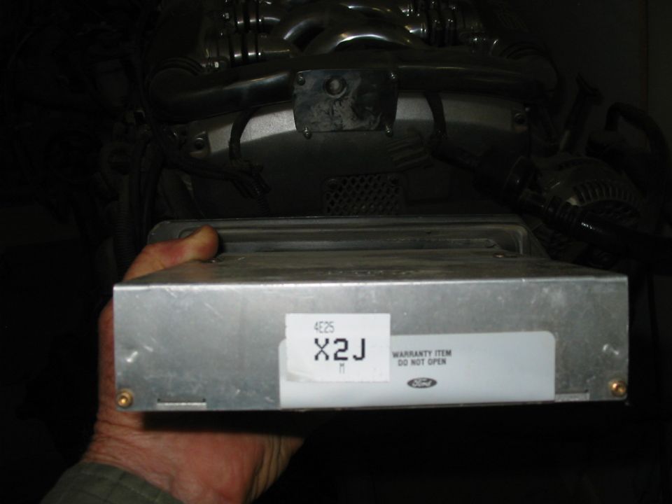Hand holding a Ford ECU labeled X2J with warranty item do not open sticker