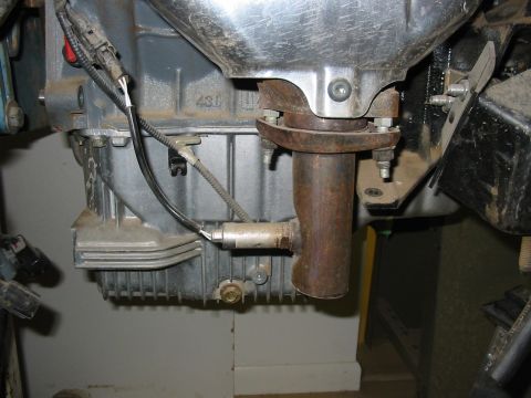 1993 Ford Taurus - Underside close-up of a cast aluminum transaxle or transmission case marked "430", with a rusty exhaust pipe bolted through a two-piece fla…