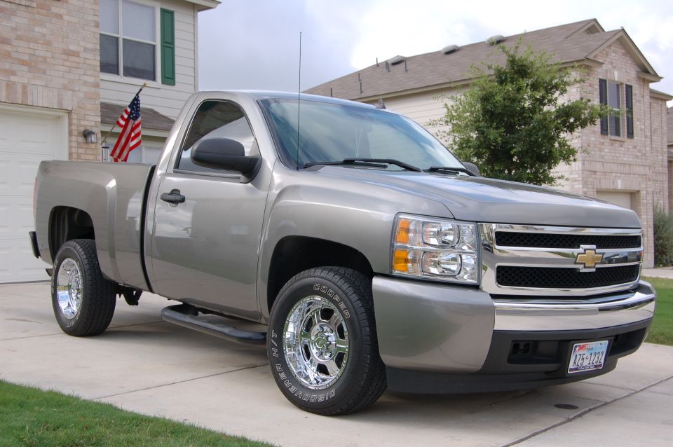 Silver pickup truck parked in driveway, American flag in bed