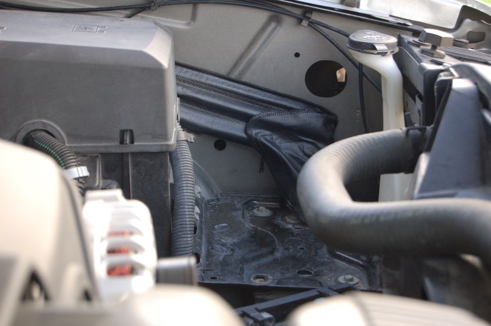 Engine bay with hoses, wiring, and a black cover
