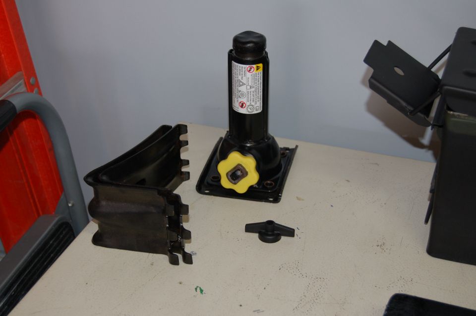 Car jack, yellow knob, and black plastic parts on a table next to a ladder