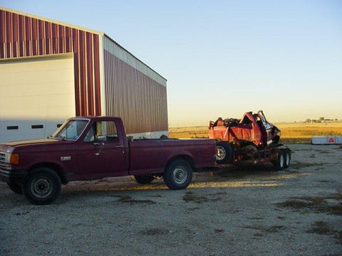 1992 Ford Bronco - A maroon Ford F-250 pickup truck tows a red vehicle on a trailer next to a barn under a clear sky.