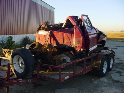 1992 Ford Bronco - A heavily damaged red pickup truck cab is loaded onto a trailer, awaiting transport or salvage.