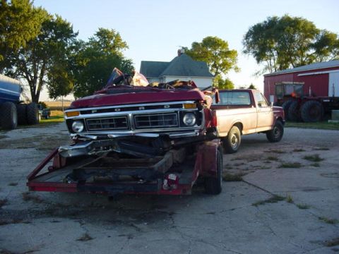 1992 Ford Bronco - Damaged red Ford truck loaded onto a trailer, with another truck in the background.