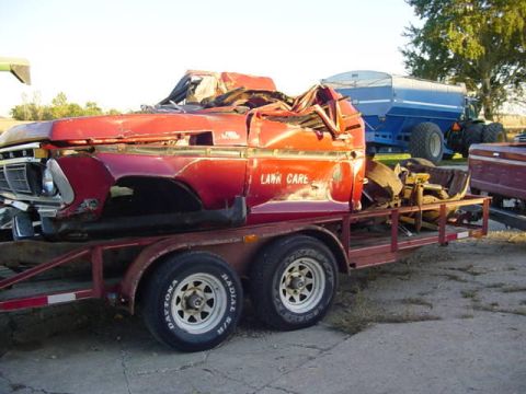 1992 Ford Bronco - A heavily damaged red truck cab, possibly from the early to mid-1970s, is loaded onto a trailer.