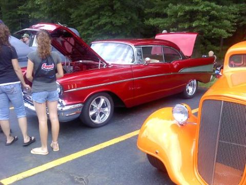 1970 Ford Ranchero - A red 1957 Chevrolet Bel Air coupe is displayed with its hood open, alongside an orange hot rod at an outdoor event.