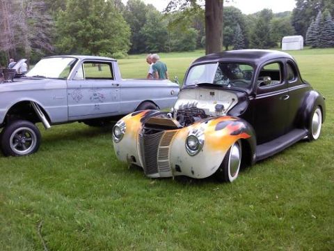 1970 Ford Ranchero - Two vehicles, a hot rod coupe and a pickup truck, are parked on a grassy field with trees in the background.