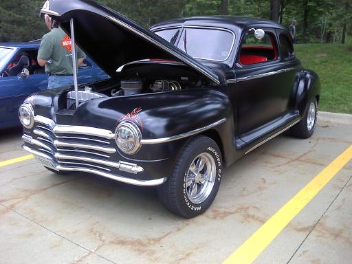 Black coupe with hood open, red interior, and chrome grille