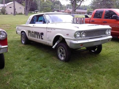 1970 Ford Ranchero - Custom drag car with 'FUGITIVE' lettering and hood stacks sits on grass next to a red truck.