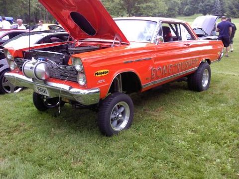 1970 Ford Ranchero - A modified orange car with its hood up sits on a grassy field next to other vehicles.