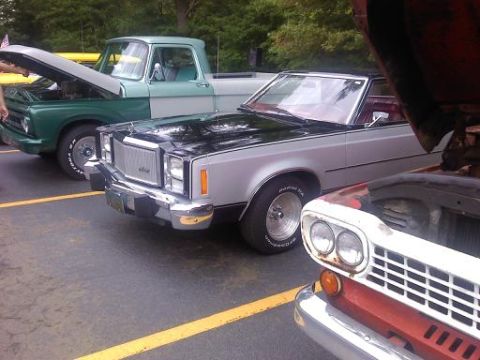 1970 Ford Ranchero - A silver and black car with a red interior is parked next to a green truck and a red car.