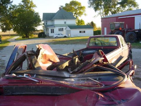 1992 Ford Bronco - This heavily damaged red pickup truck is shown from the front, with its windshield and hood severely crushed.