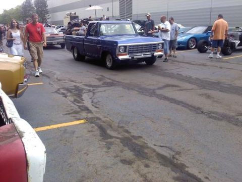 1970 Ford Ranchero - A blue pickup truck is parked on a lot with other vehicles and people around.
