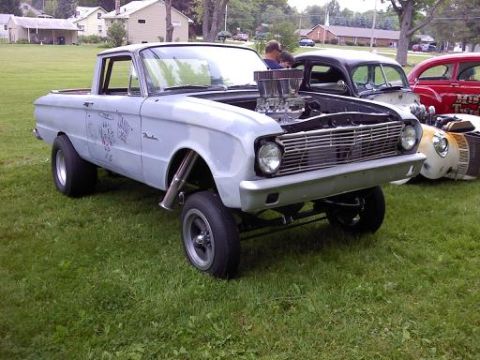 1970 Ford Ranchero - This heavily modified pickup truck features a prominent engine and custom exhaust pipes, parked alongside other vehicles.