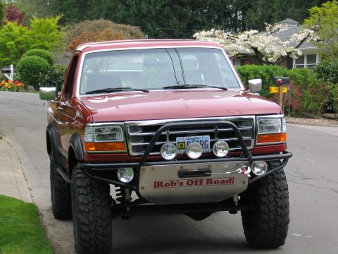 1989 Ford Bronco - This red Ford Bronco features a custom brush guard and off-road lights, with a "Rob's Off Road" decal on the skid plate.