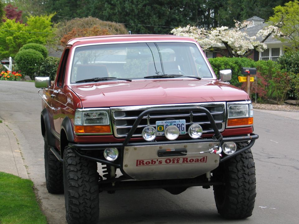 Red Ford Bronco with a brush guard and winch, parked on a residential street