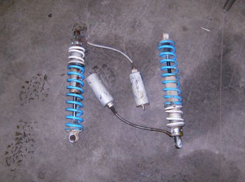 2000 Ford E350 - Two shock absorbers and their associated reservoirs are shown on a concrete surface.